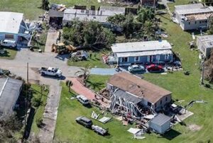 Una familia de Florida limpiando escombros en su propiedad tras el paso de dos huracanes, con una casa parcialmente destruida y un generador portátil en uso, reflejando la falta de electricidad en la zona.